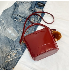 Detail view of burgundy quilted bucket bag with plush pom-pom and shoulder strap