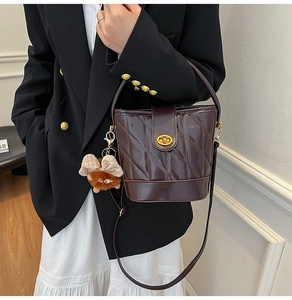 Detail of dark brown quilted bucket bag with gold hardware and plush monster charm