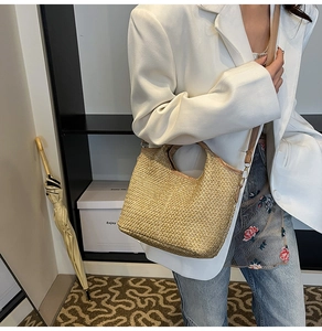 Detail of woven straw bucket bag with brown leather handles and adjustable shoulder strap