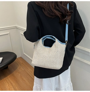 Detail of woven straw bucket bag in off-white with blue leather strap on model