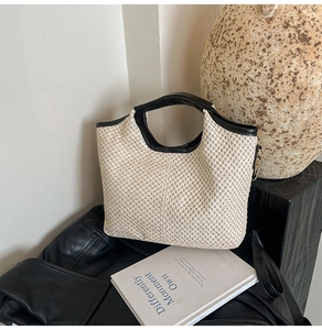 Detail of cream woven straw bucket bag featuring black leather trim and gold metal rings