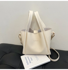 Detail view of cream bucket bag with litchi grain texture and gold FASHION lettering
