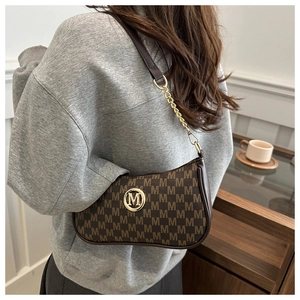 Brown leather armpit bag with golden chain strap shown on model in stylish interior setting