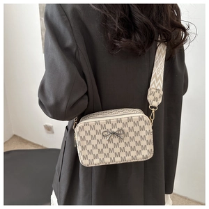 Close-up of cream crossbody bag with M-pattern logo, black bow, and wide strap on model