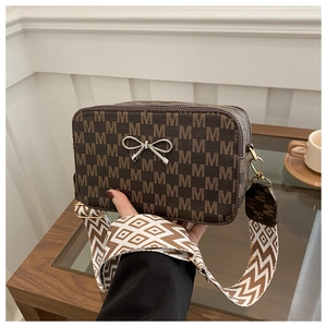 Detail shot of brown leather crossbody bag with wide patterned strap and metal hardware