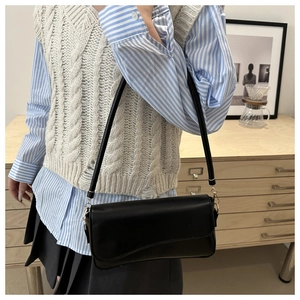 Minimalist black PU leather underarm bag worn by a model in a cozy indoor setting