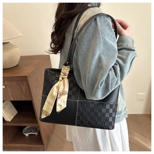 Detail of a large black checkerboard tote bag with an elegant silk scarf on the handle