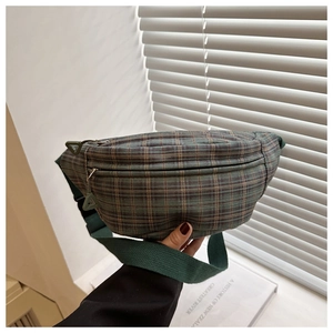 Détail d'un sac bandoulière vert à carreaux tenu à la hand près d'une fenêtre
