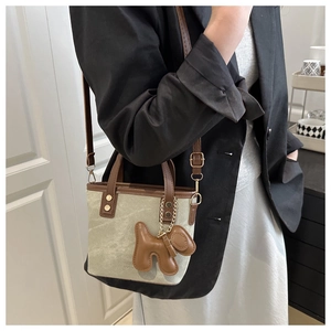 Detail of canvas bucket bag with brown leather trim and a cute dog charm accessory