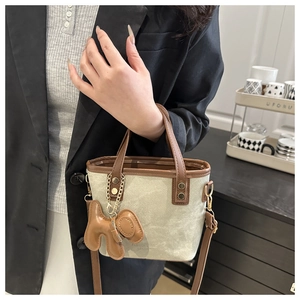 Detail of canvas and brown leather crossbody bucket bag with dog-shaped charm
