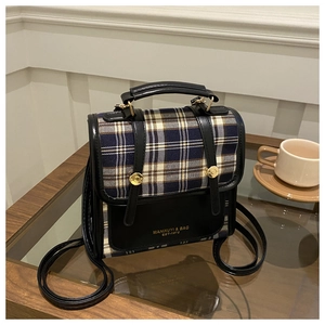 Détail d'un sac vintage à carreaux style collège avec logo doré et finitions cuir
