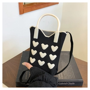 Close-up of a black knitted mini bag featuring white heart patterns on an art book