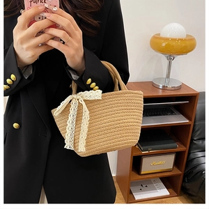 Détail d'un sac cabas en paille tissée avec un nœud en dentelle blanche et franges