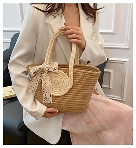 Close-up of handmade straw tote bag with white lace bow and contrasting handles