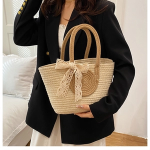 Detail of woven straw tote bag featuring delicate cream lace bow and contrast circular patch