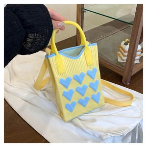 Detail of yellow knit handbag showing blue heart patterns and textured woven fabric