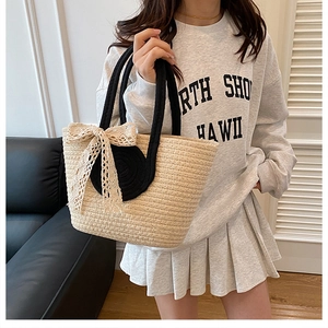 Detail of woven straw tote bag featuring a beige lace bow and black rope handles