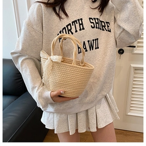 Détail du sac cabas en paille tissée avec accessoire nœud en dentelle blanche sur l'anse