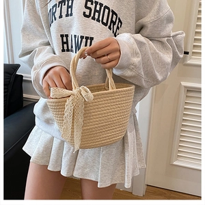 Détail de la texture en paille tressée et du nœud en dentelle blanche sur le sac cabas