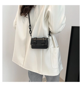Detail view of mini black crossbody bag with double buckles and chain strap on model