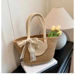 Close-up of woven straw tote bag featuring a cream lace bow and sturdy rope handle