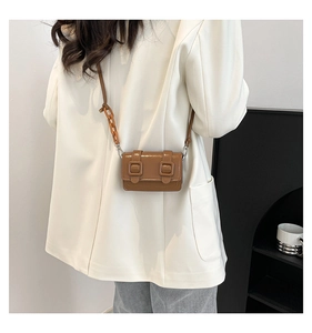 Close-up of brown glossy mini crossbody bag with amber resin chain worn on white blazer