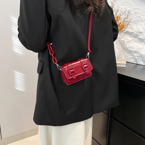 Glossy red mini crossbody bag with chain strap shown on model in black suit