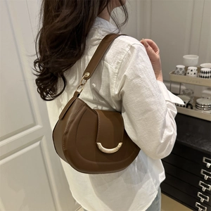 Sacoche selle minimaliste en cuir marron avec boucle dorée portée par un mannequin