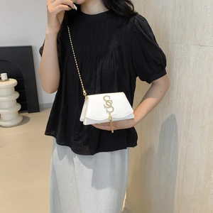 Petit sac carré blanc en cuir avec boucle en S dorée et pompon porté par un mannequin