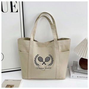 Detail view of large beige canvas tote bag with tennis theme print in a cozy setting