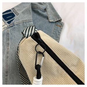 Detail of beige corduroy pillow bag featuring black metal zipper and striped woven strap