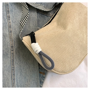 Close-up of beige corduroy shoulder bag with striped woven strap and zipper detail