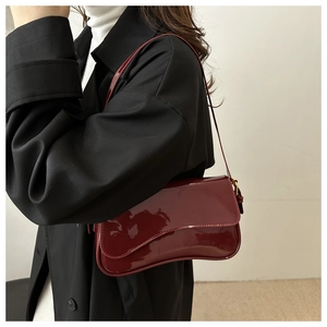 Model wearing a burgundy patent leather underarm bag with a glossy finish and slim strap
