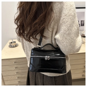 Detail view of a black glossy patent leather handbag with silver zippers and shoulder strap