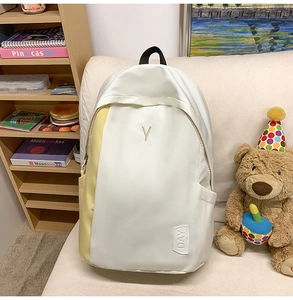 Close-up of minimalist cream and yellow backpack with Y embroidery on fabric sofa