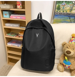 Detailed view of black canvas backpack featuring minimalist white letter Y and leather patch