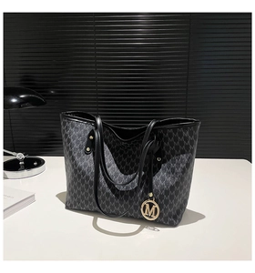 Detail der grauen Totebag mit M-Muster, Print und rundem goldenem Metallanhänger