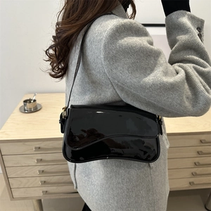 Glossy black patent leather underarm bag with wavy flap and adjustable gold hardware buckle