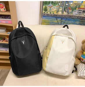Detail of minimalist nylon backpacks in black and beige showing metal Y logo and side pockets