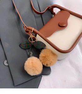 Close-up of contrast crossbody bag with decorative plush cherry keychain on gray suit