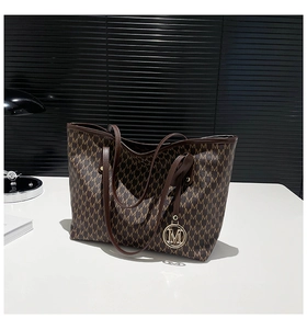 Detailansicht der großen Tote Bag mit braunem M-Muster und Metall-Logo-Anhänger