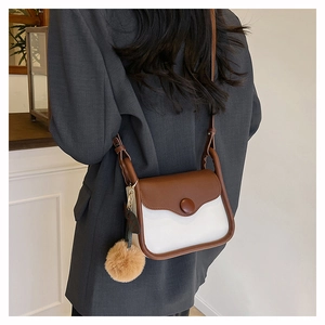 Brown and white contrast crossbody bag with soft plush ball charm worn with a grey blazer