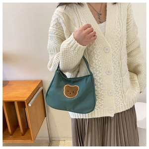 Detail of green baguette bag featuring a textured brown plush bear embroidery patch