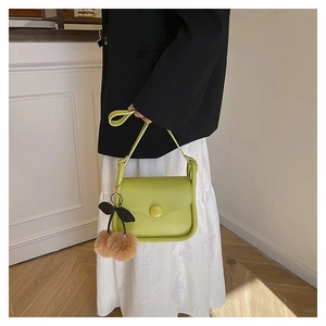 Detail of avocado green leather crossbody bag with a cute cherry plush charm accessory