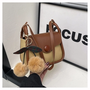 Close-up of contrast color crossbody bag featuring a cute plush cherry charm detail