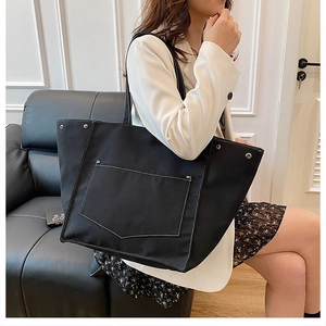 Détail d'un grand sac cabas en toile noire avec surpiqûres blanches et poche avant