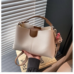 Détail du sac seau beige texture litchi avec garniture marron et breloque ours en peluche