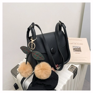 Detail of a black leather handbag with a cherry pom-pom charm on a striped suitcase