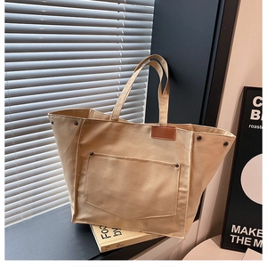 Détail du sac cabas en toile beige montrant le tissu texturé et l'étiquette en cuir brun