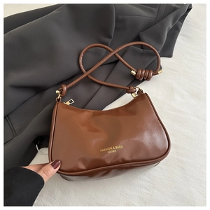 Close-up of brown vintage leather shoulder bag with gold logo on dark gray suit fabric